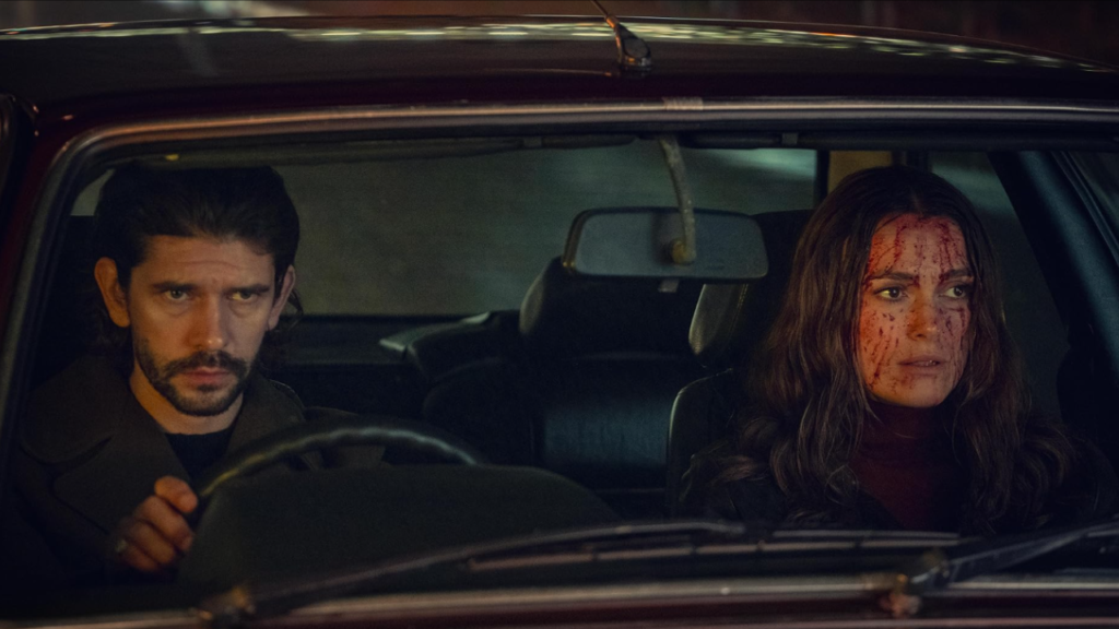 Ben Whishaw and Keira Knightley in an intense scene from Netflix’s spy thriller Black Doves. The two characters are seated in a car at night, with Knightley’s face streaked with blood, reflecting the suspenseful and dangerous tone of the series